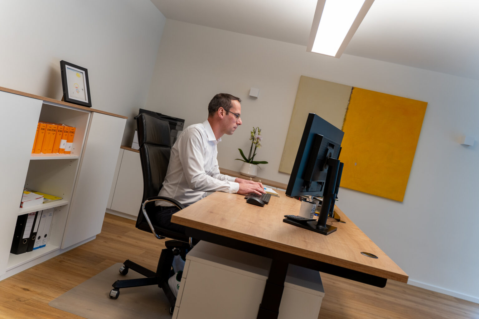 Hendrik Lienemann sitzt in einem modernen Büro an einem Holzschreibtisch und arbeitet konzentriert am Bildschirm